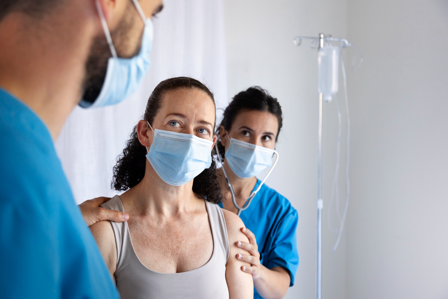A female with medical mask having an IV therapy, with nurses around her