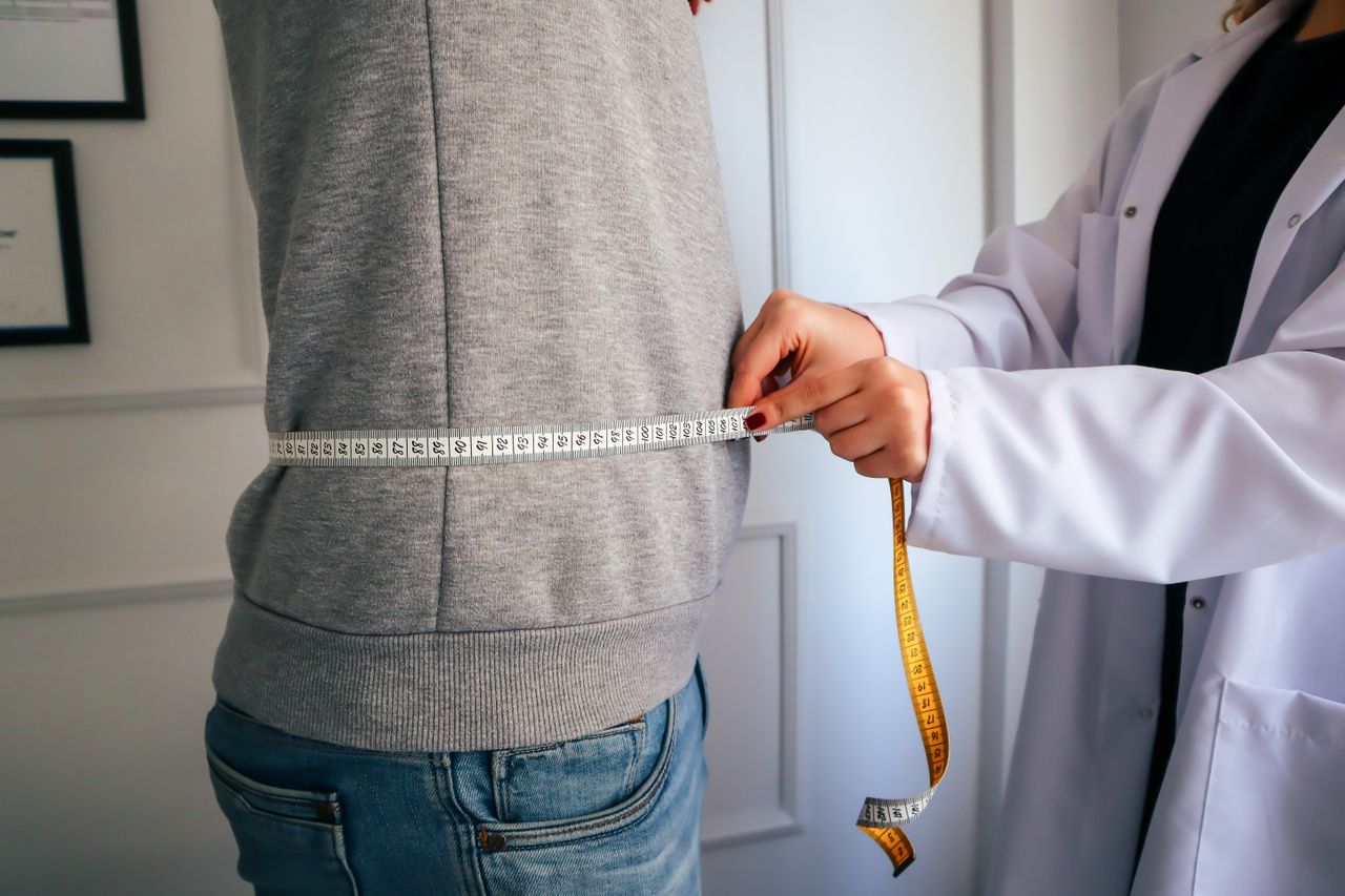 A nutritionist measuring a patient's waist using a tape.