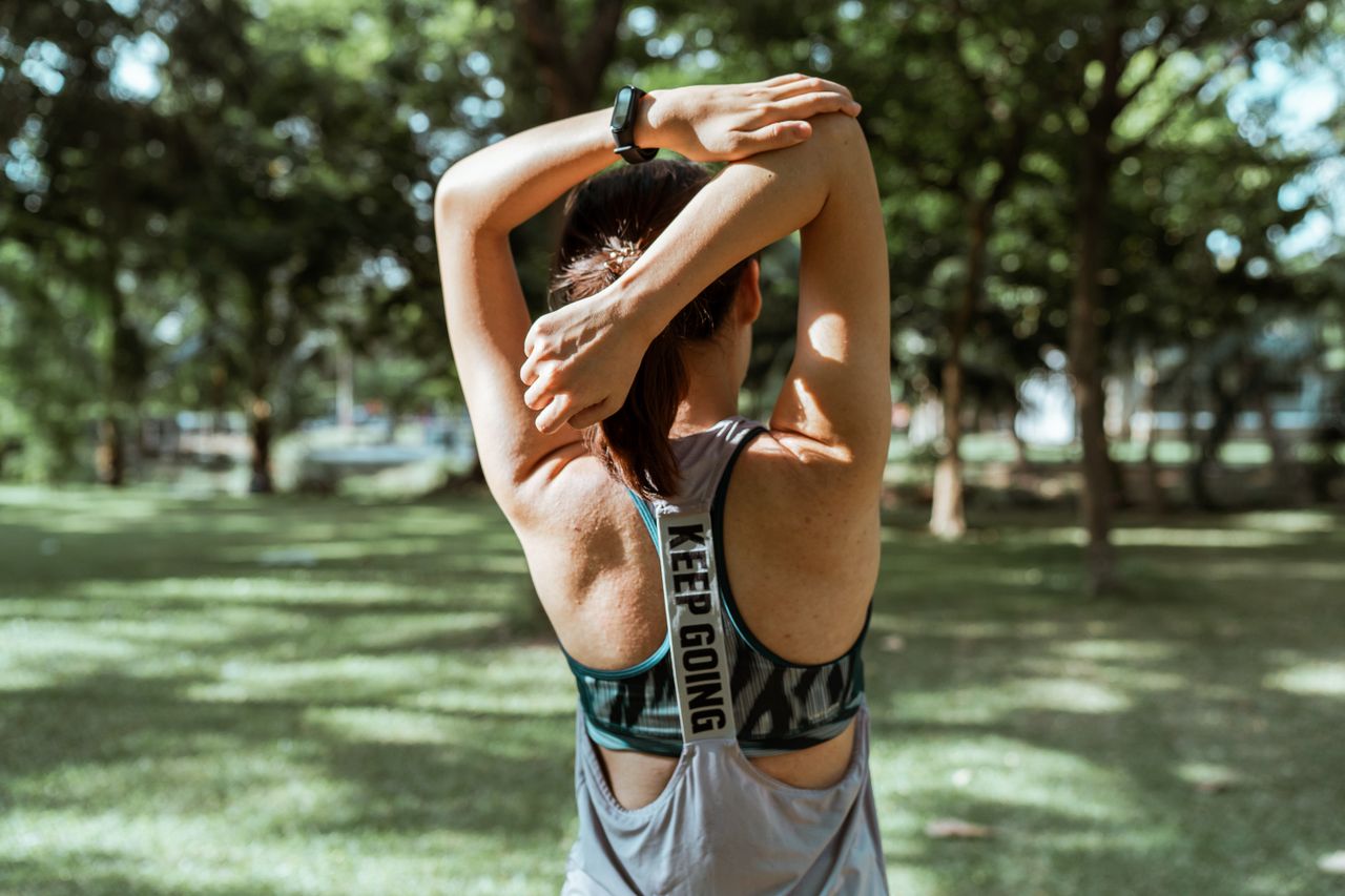 Fitness enthusiast stretches outdoors in a sunny park, promoting active lifestyle and wellbeing.